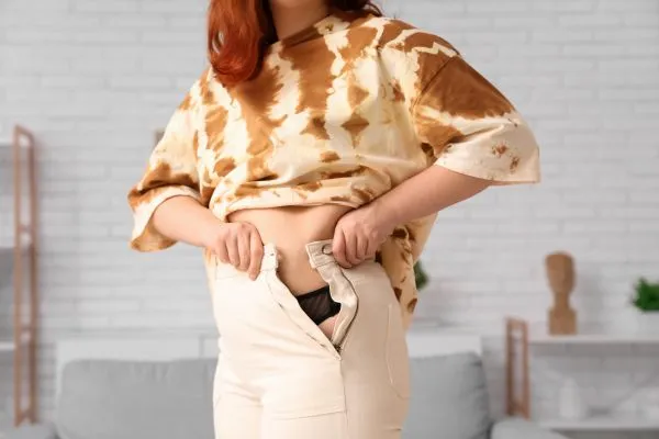 Image of woman trying to do her trousers up after pregnancy weight gain Haslemere